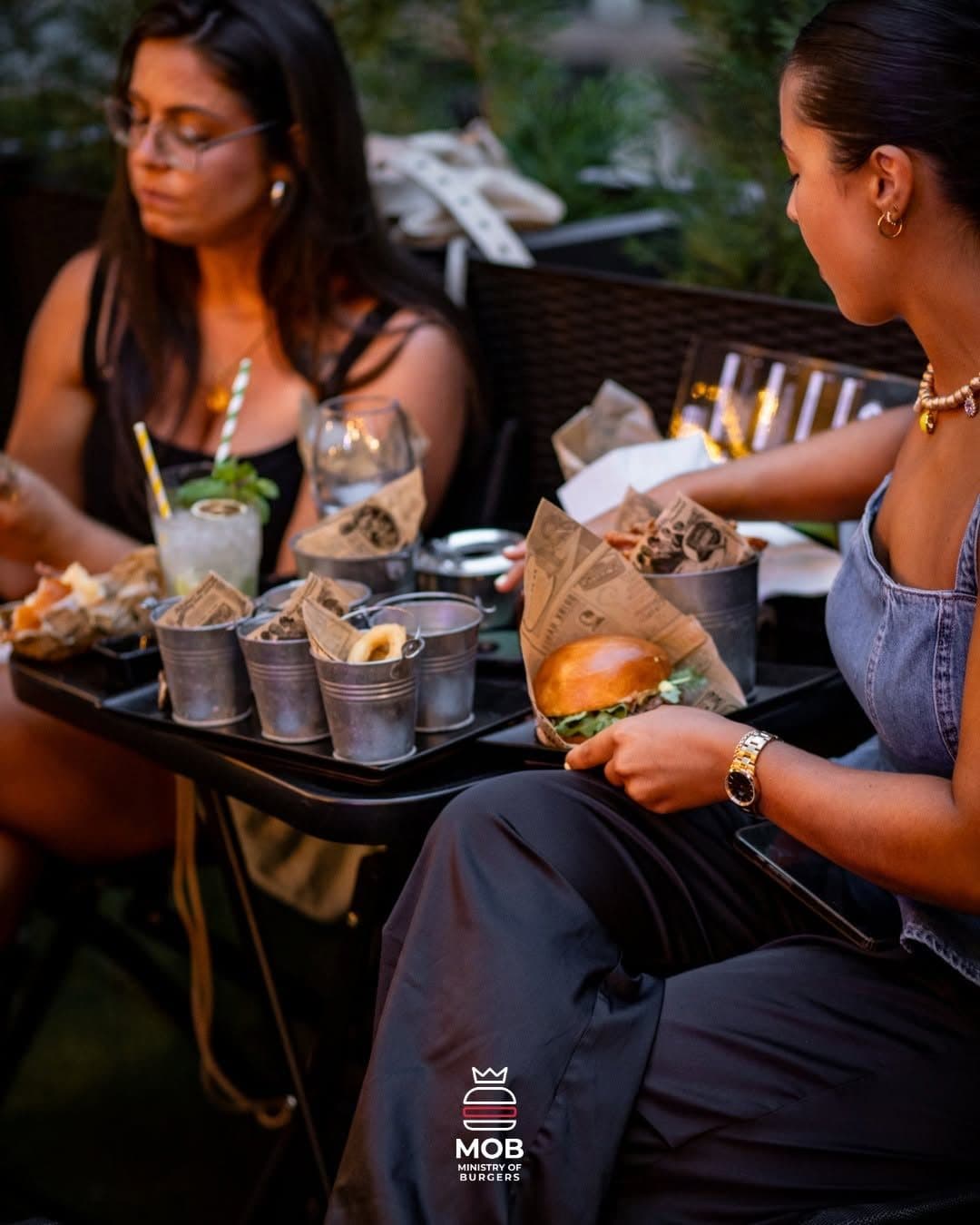 Duas amigas na esplanada com tabuleiros de burgers e batatas